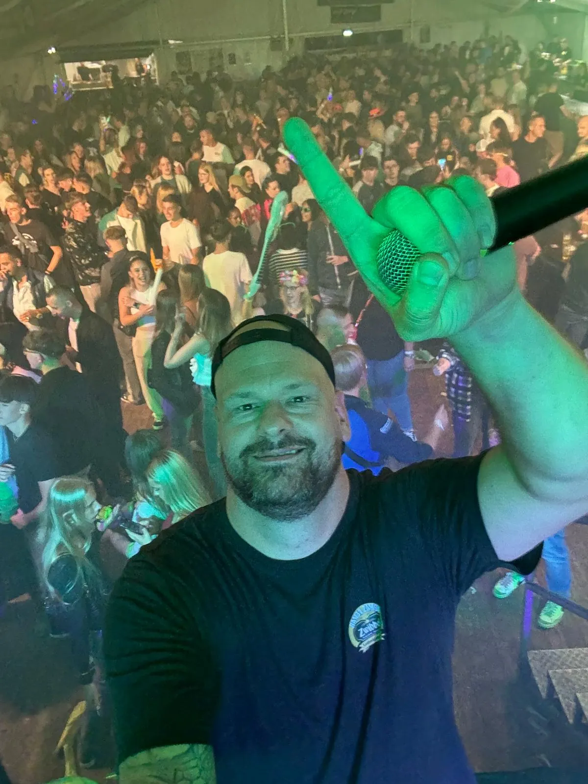 Marian am DJ-Pult vor einer vollen Tanzfläche im grünen Bühnenlicht